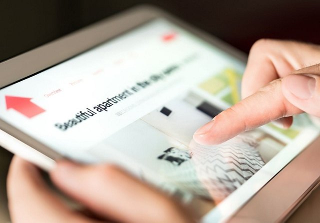 Close-up of a person's fingers browsing a real estate website on a tablet.